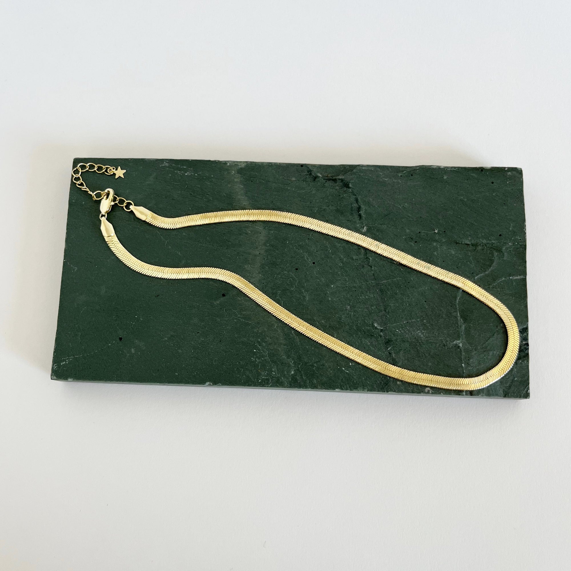 Snake chain necklace in gold on green rock. 